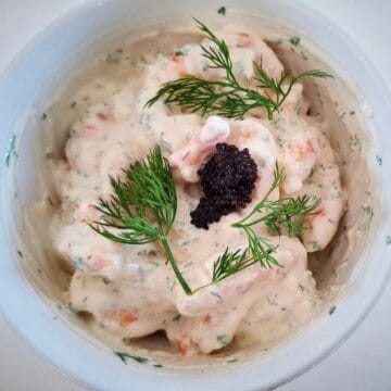 prawn shrimp skagen with lump fish caviar and fresh dill on top in a white bowl on a white table