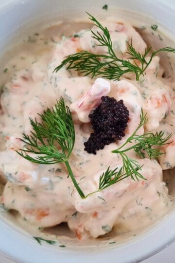 prawn shrimp skagen with lump fish caviar and fresh dill on top in a white bowl on a white table