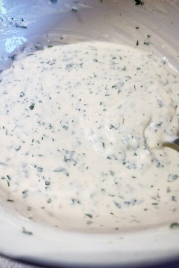 Mixing yoghurt mint dressing with a spoon in a white bowl.