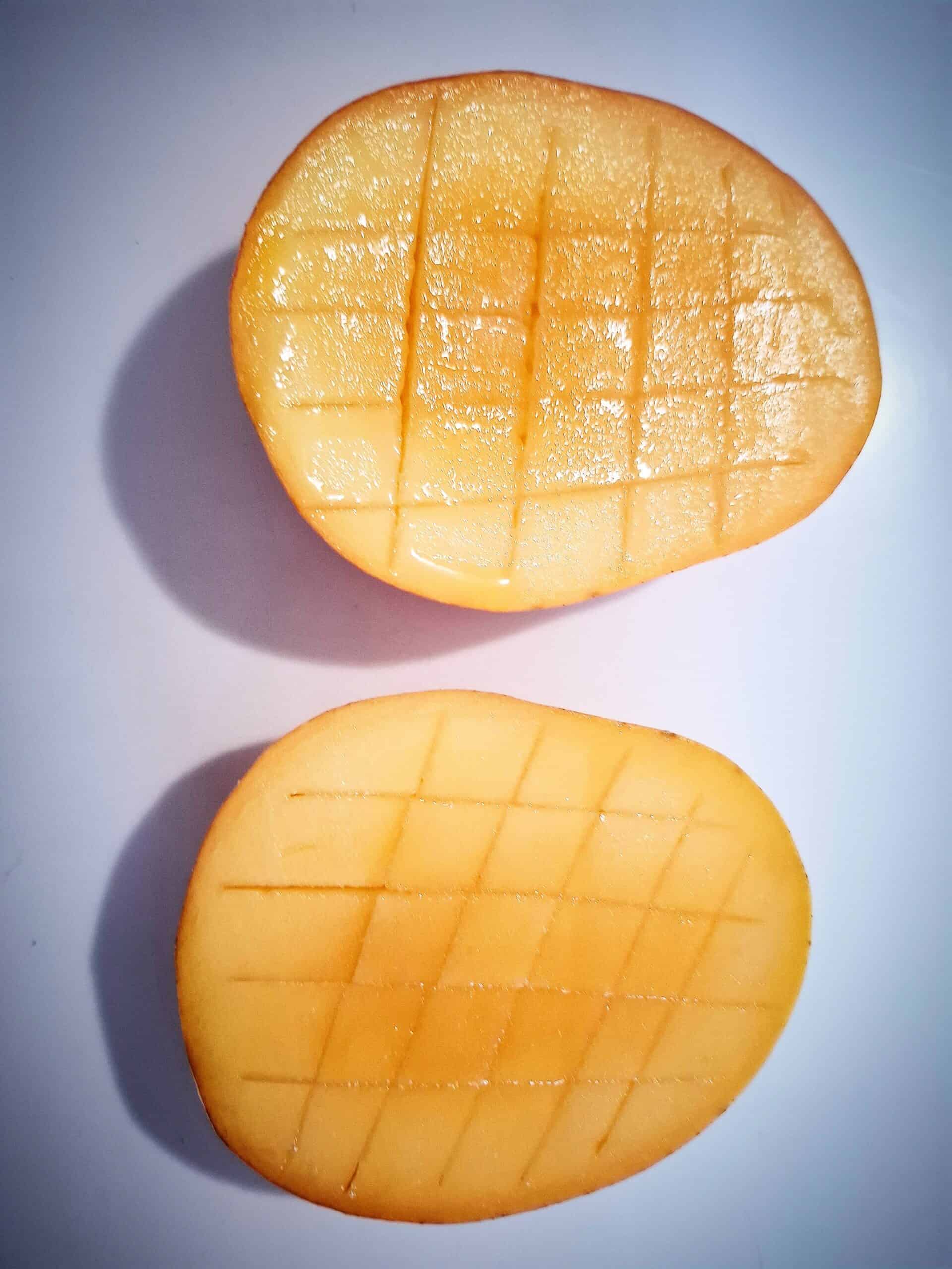 Two mango cheeks with a knife scored crisscross pattern in the flesh on top of a white bench