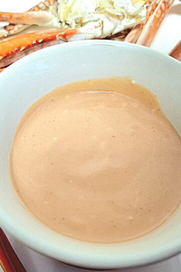 Seafood cocktail sauce in a round ramekin on a white plate with crab pieces on it.