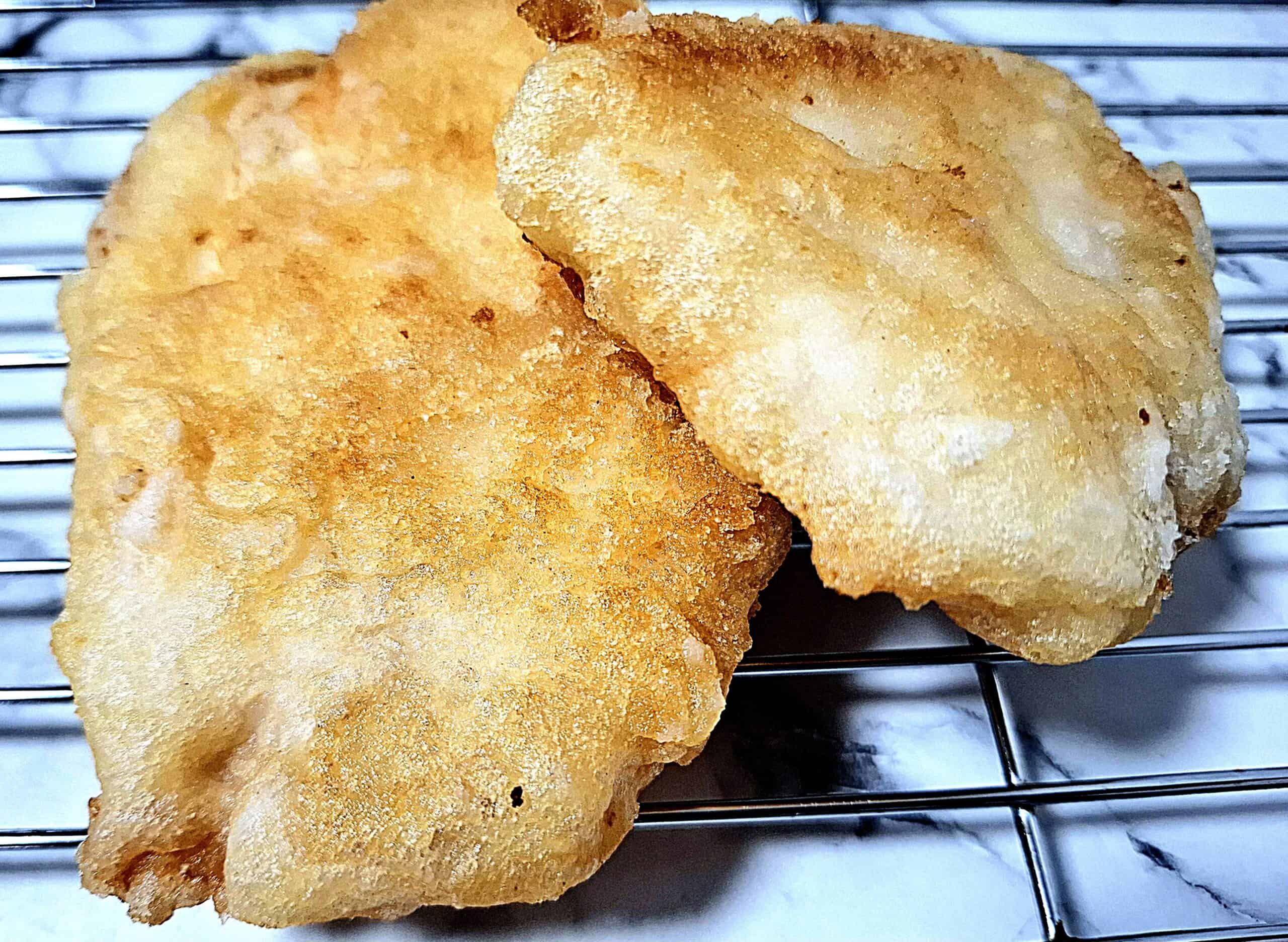 Two crispy fish tempura on a wired wrack. One piece slightly on top of the other