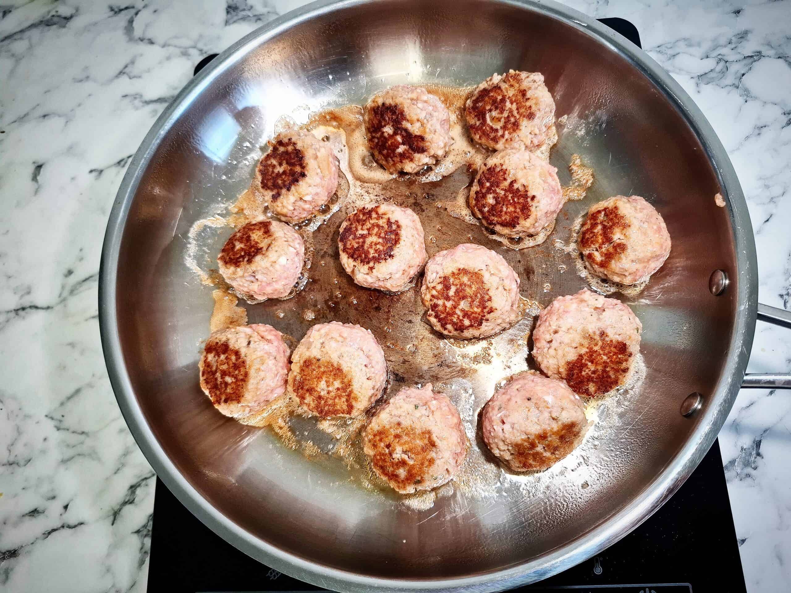 Frying meatballs until golden brown and caramelized in a stainless steel frying pan