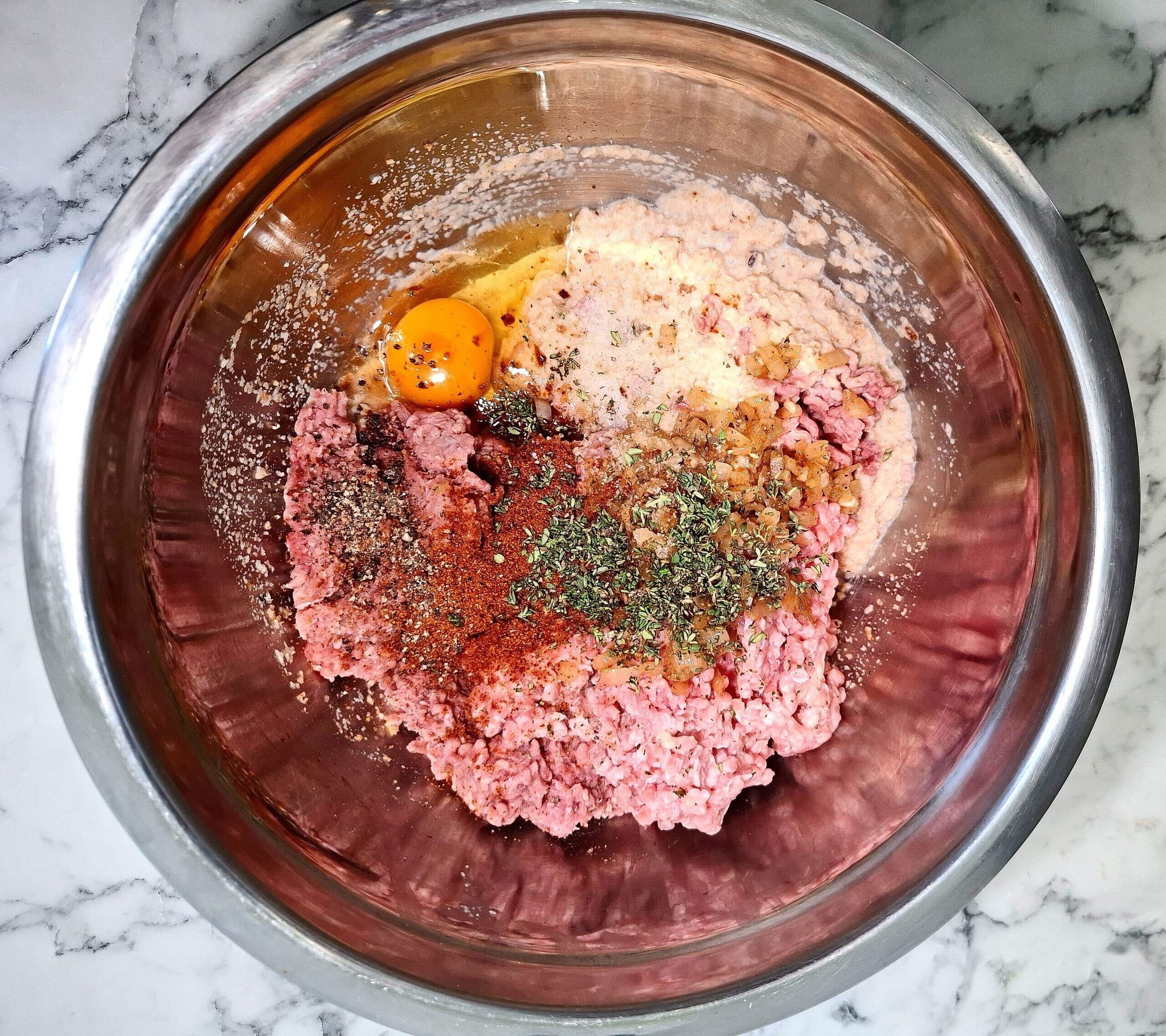 Meatballs ingredients in a stainless steel mixing bowl