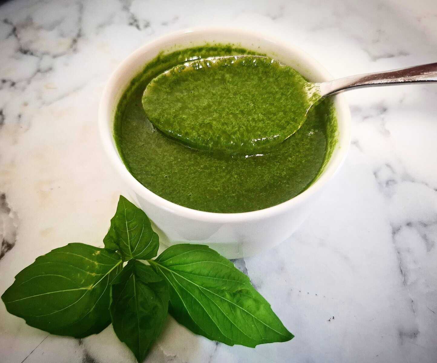 Basil garlic oil in a white ramekin with a spoon holding up some of the oil. Fresh basil leaves in front of it