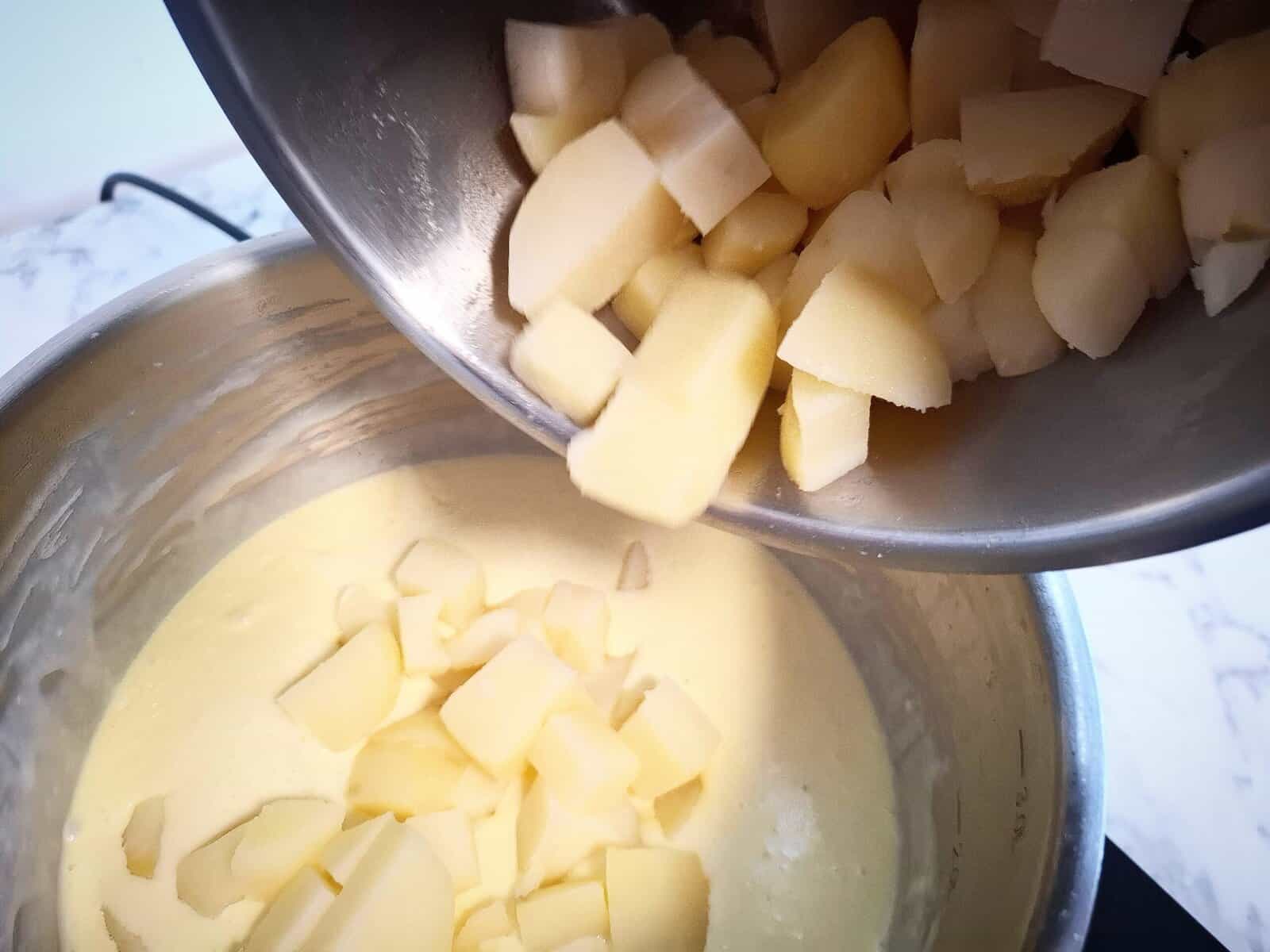 Adding cut potatoes to the creamy sauce in the saucepan