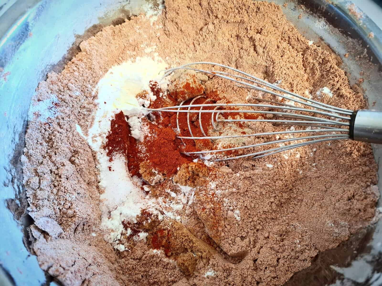 The spices for the spice coating mix are being mixed together in a stainless steel bowl with a whisk.