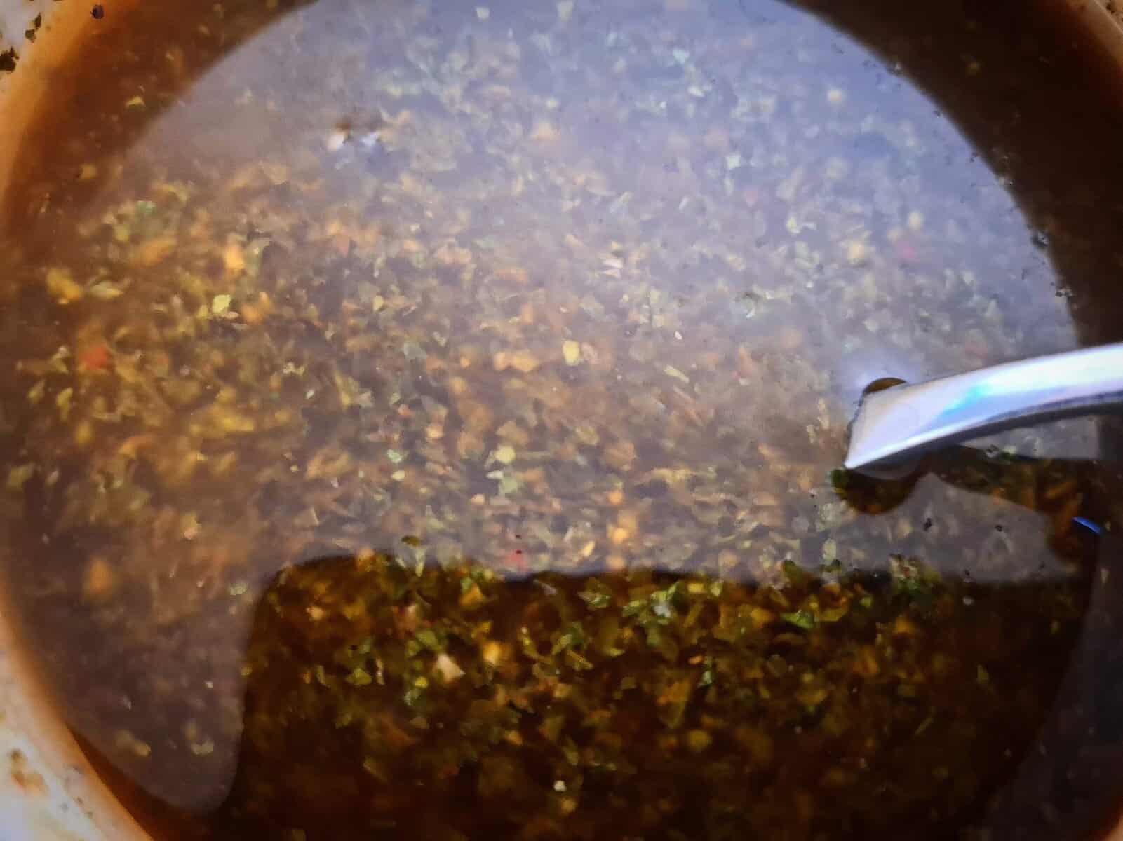 A close up picture of red chimichurri sauce in a white bowl with a spoon in it.