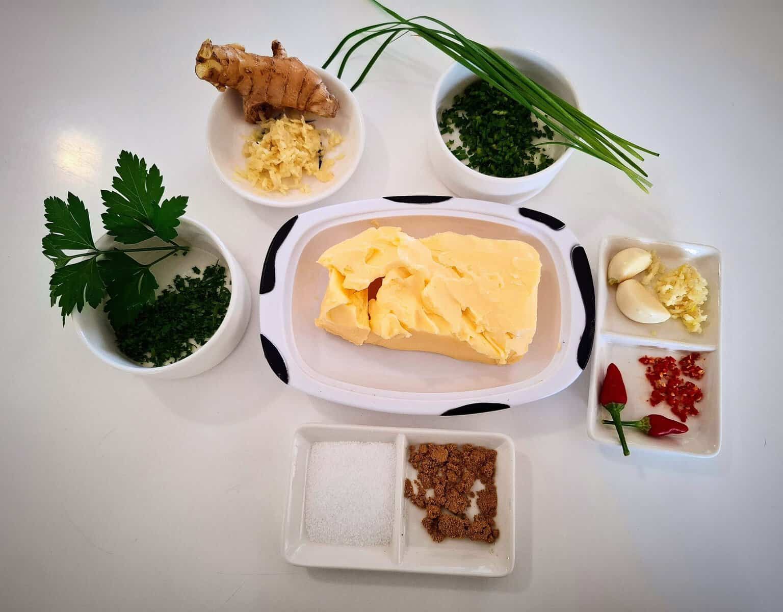 Ingredients for garlic ginger butter in ramekins on a white table top