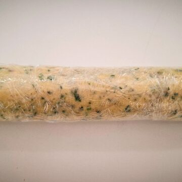 Garlic ginger butter rolled up to a log in cling wrap on a white bench top