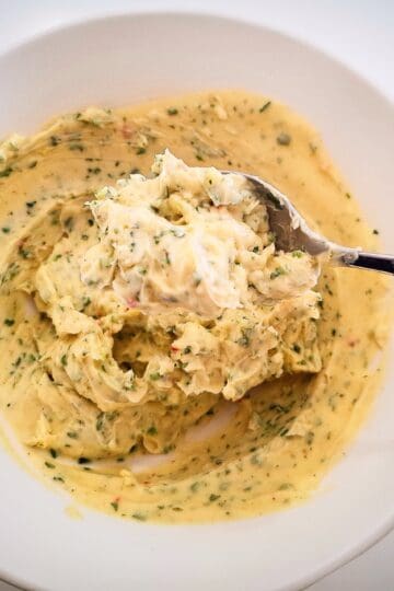 Garlic ginger butter in a white bowl on a white table with a spoon holding some butter up