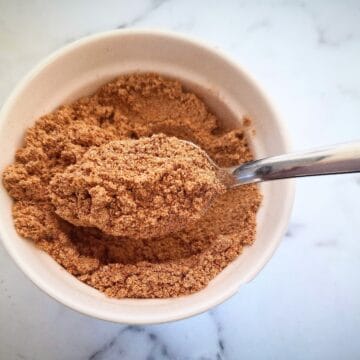 southern fried seasoning in a white ramekin with a spoon holding up spice in it on a marbled bench top