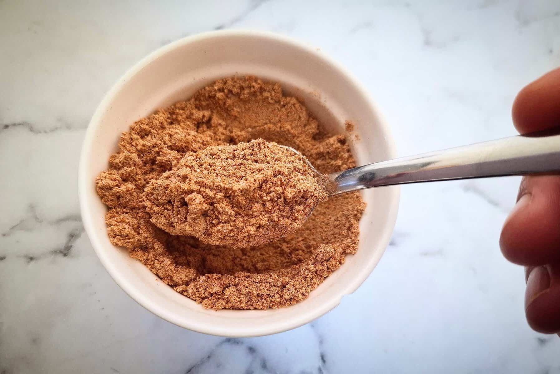 southern fried seasoning in a white ramekin with a spoon holding up spice in it on a marbled bench top