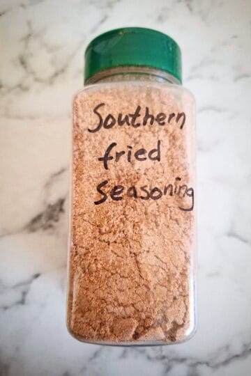 Spice coating mix in a clear spice shaker with a green lid and the words spice coating on it. A marbled background