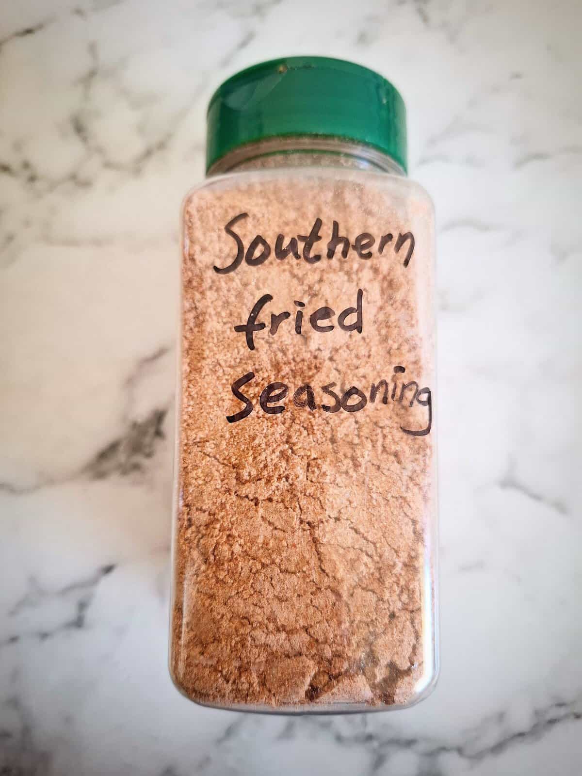 Spice coating mix in a clear spice shaker with a green lid and the words spice coating on it. A marbled background