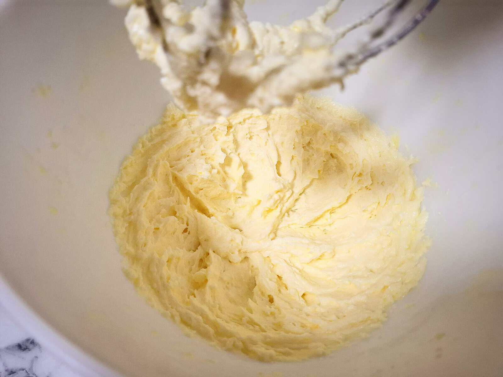 Butter and sugar has been whipped to a white and creamy mixture in a white kitchen mixer.