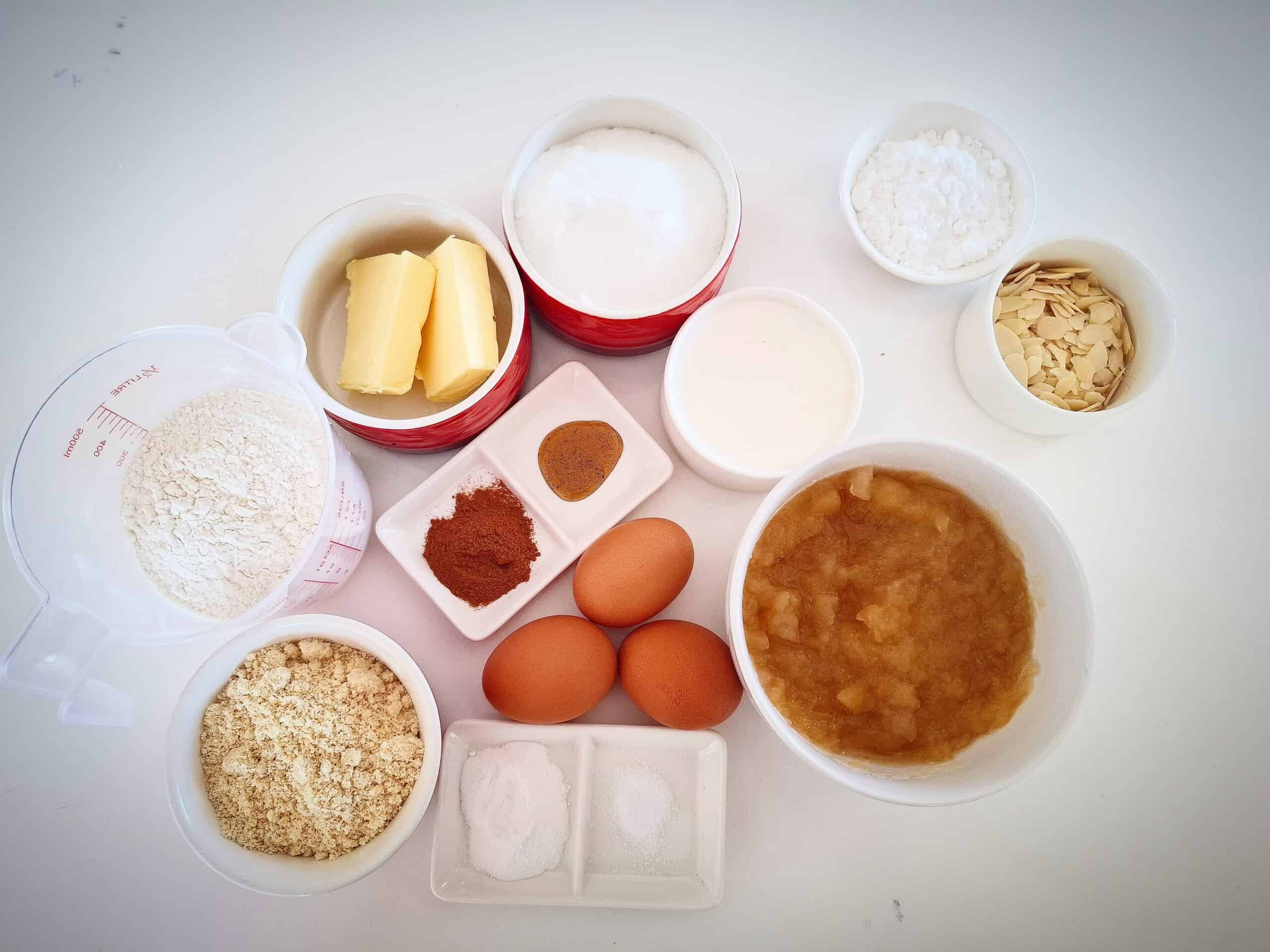 All ingredients for apple and almond cake in ramekins on a white table.