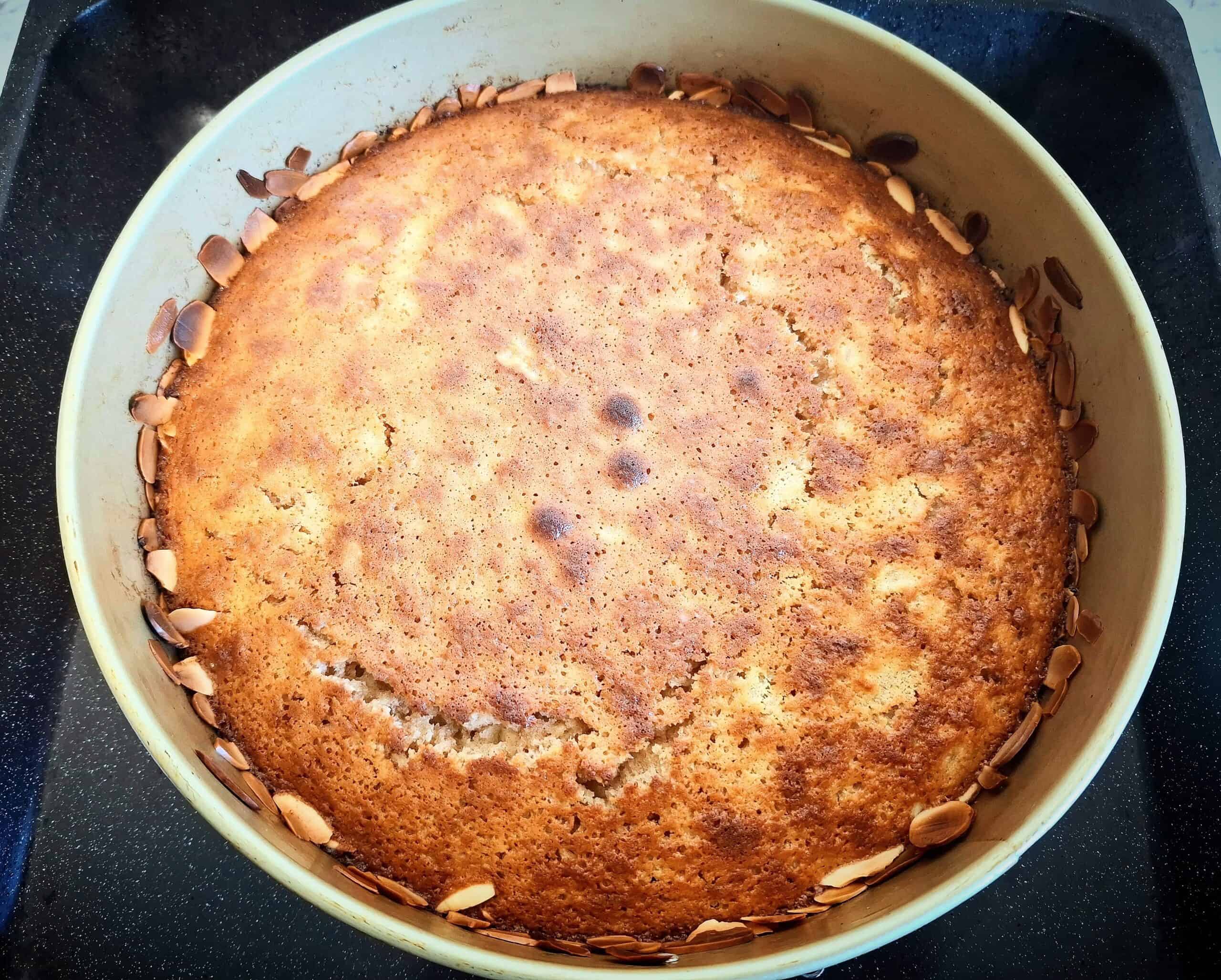 Cooked apple and almond cake in a round cake tin on a black oven tray