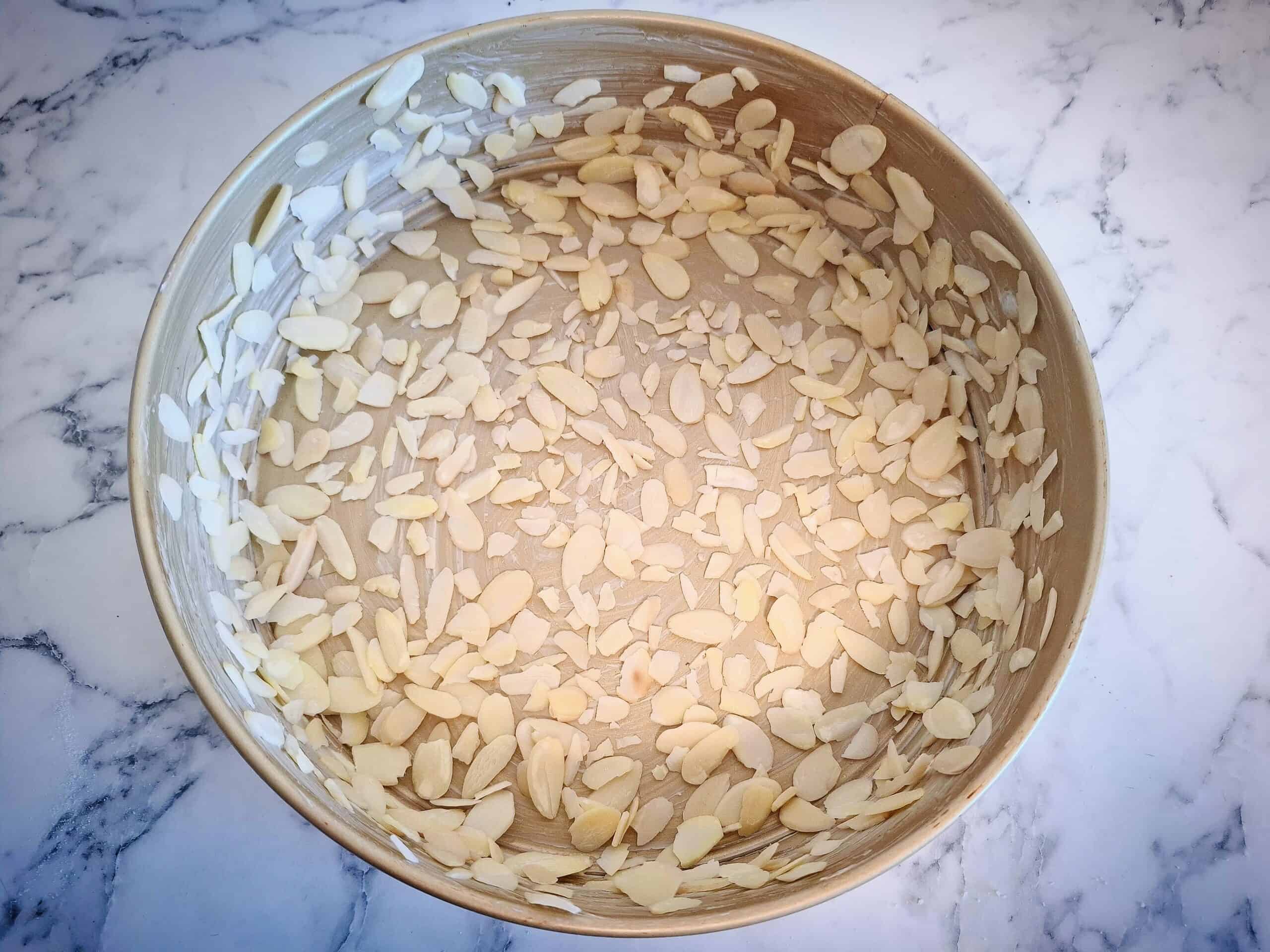 Round cake tin with a thin layer of sliced almonds.