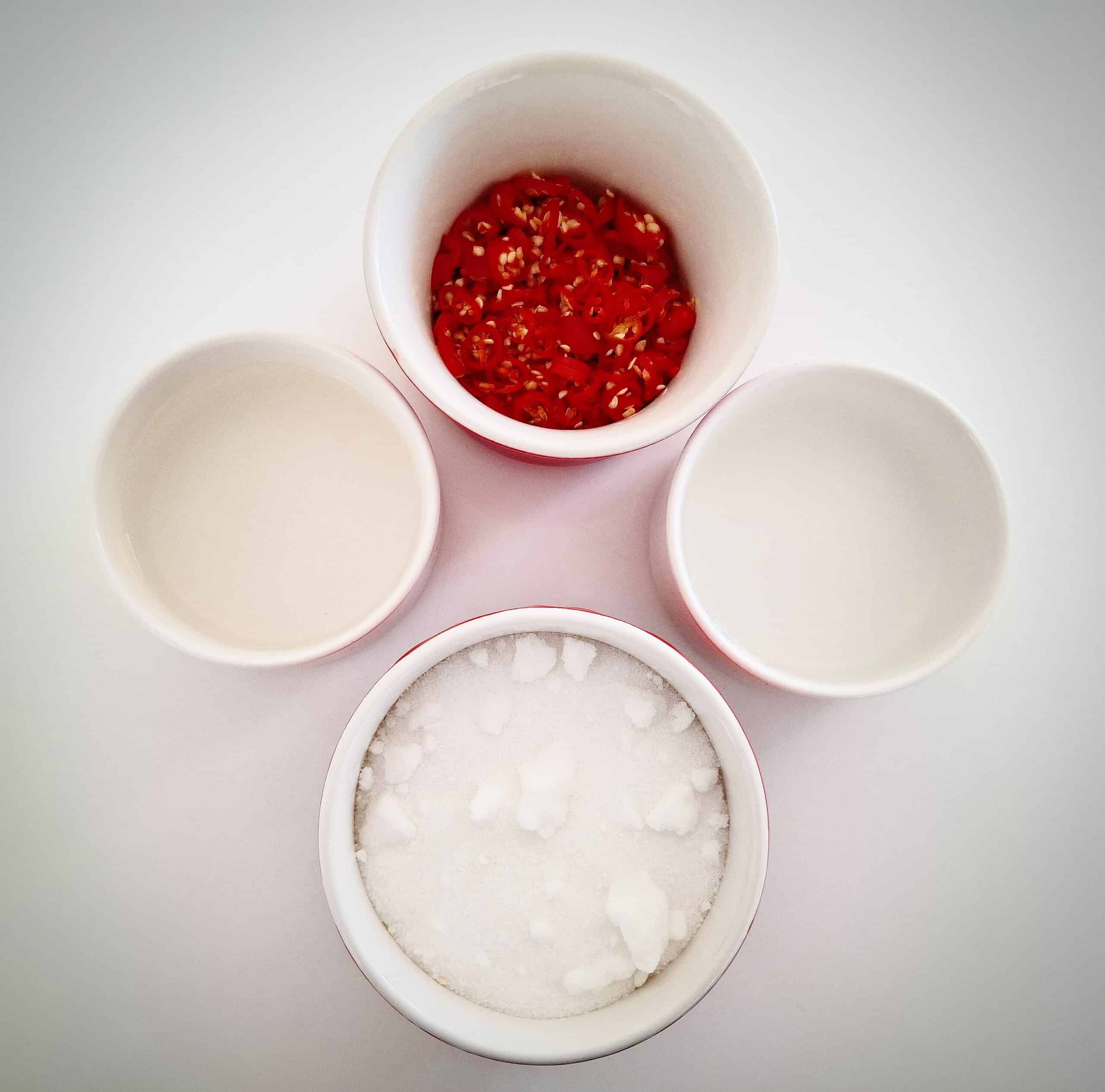 Ingredients for candied chili in ramekins on a white table top
