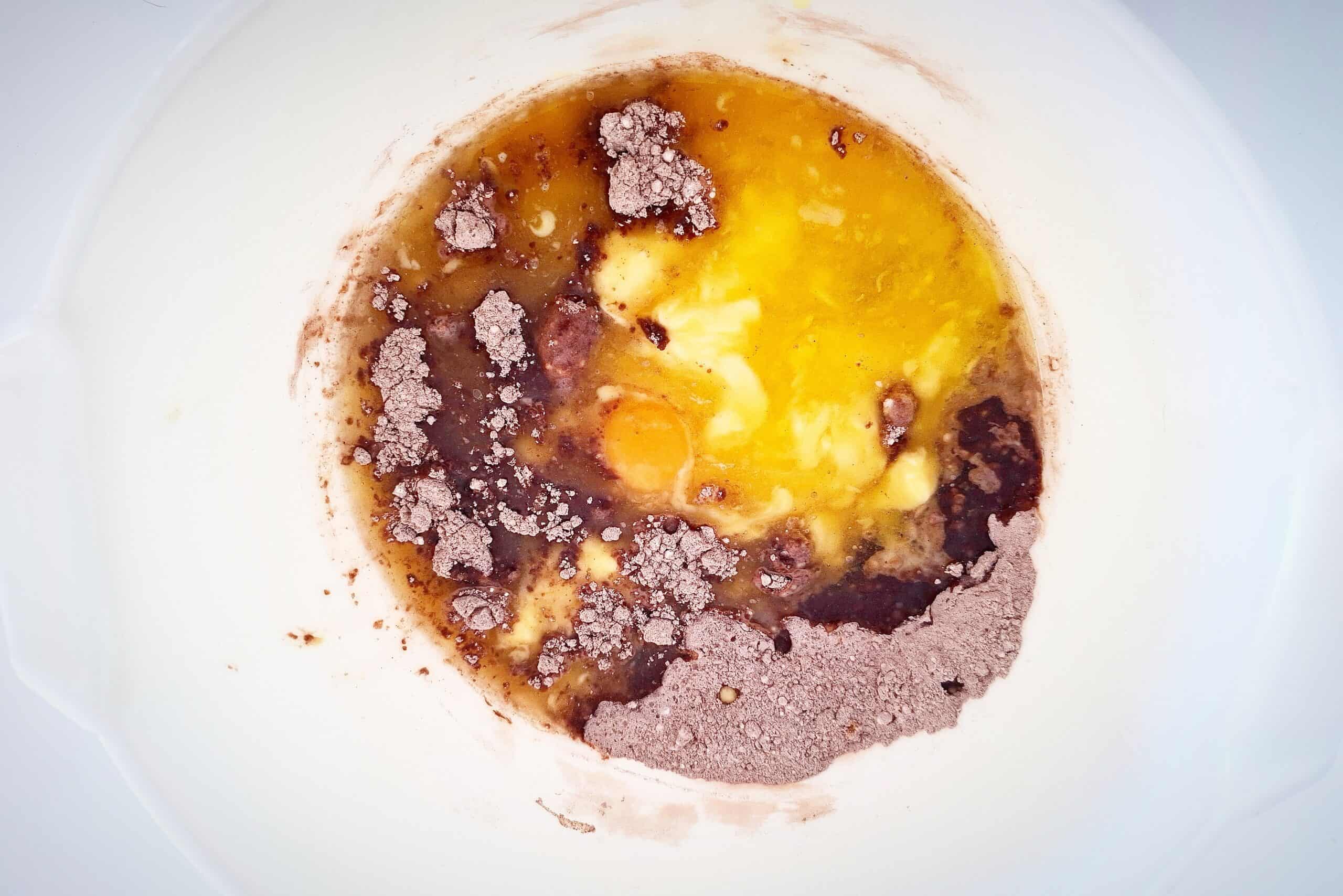 The wet ingredients for chocolate courgette cake has been added to the dry ingredients in a white bowl