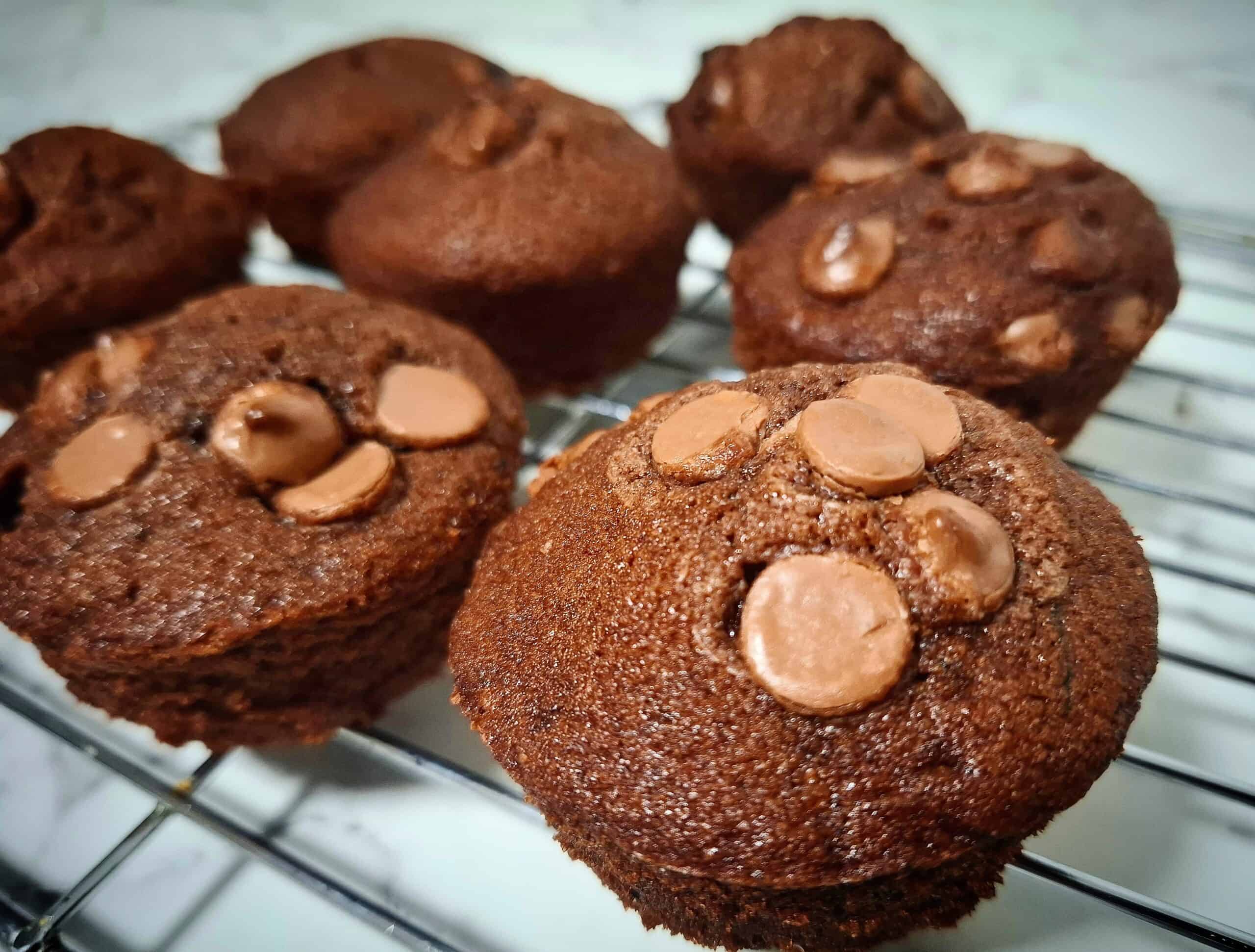 Seven courgette and chocolate muffins cooling down on a wired wrack.