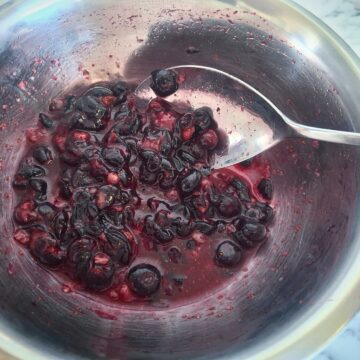 Macerated blueberries in a stainless steel bowl with a silver spoon.