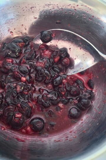 Macerated blueberries in a stainless steel bowl with a silver spoon.