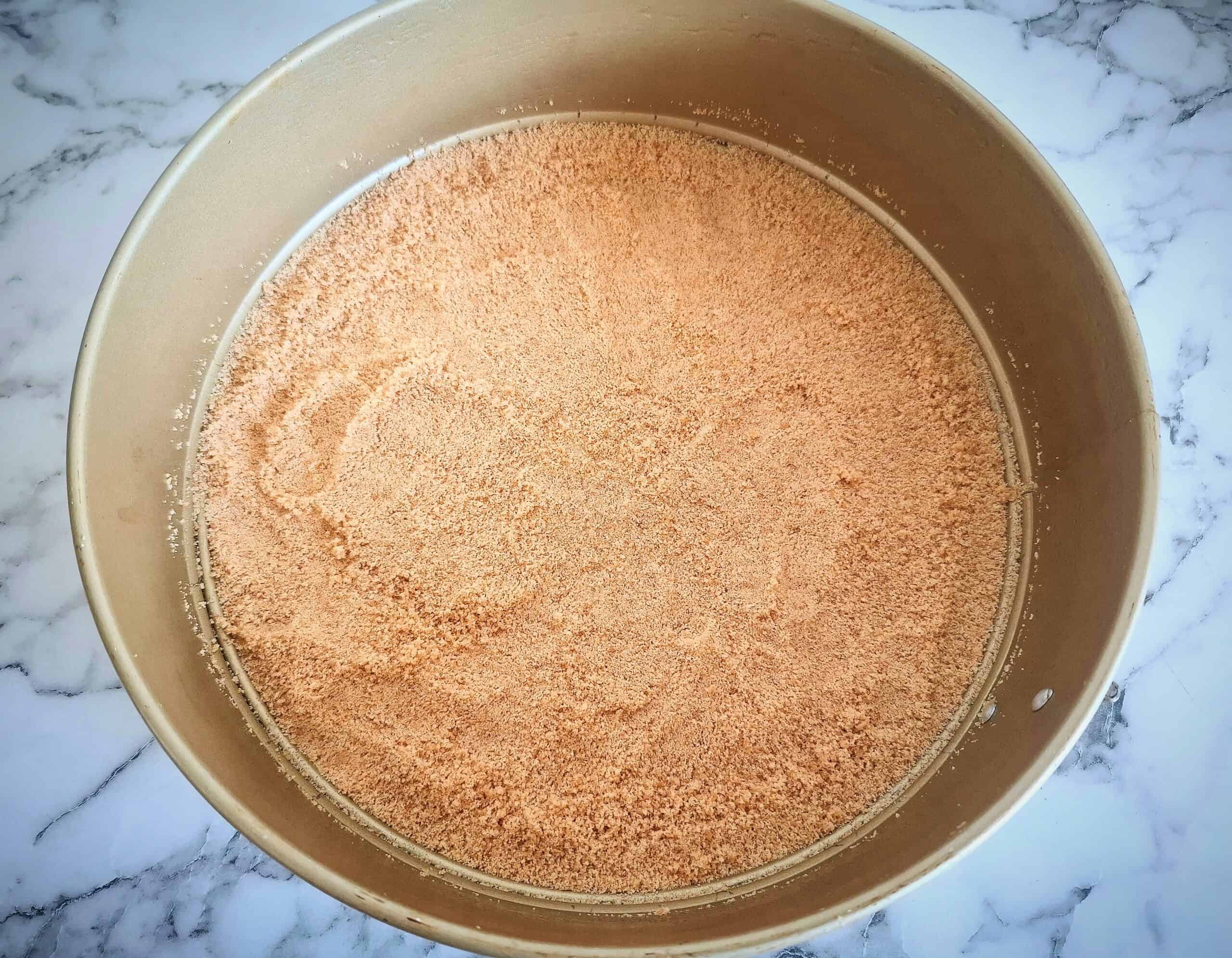 A round cake tin with removable sides with a thin layer of digestive biscuit crumbs in the bottom