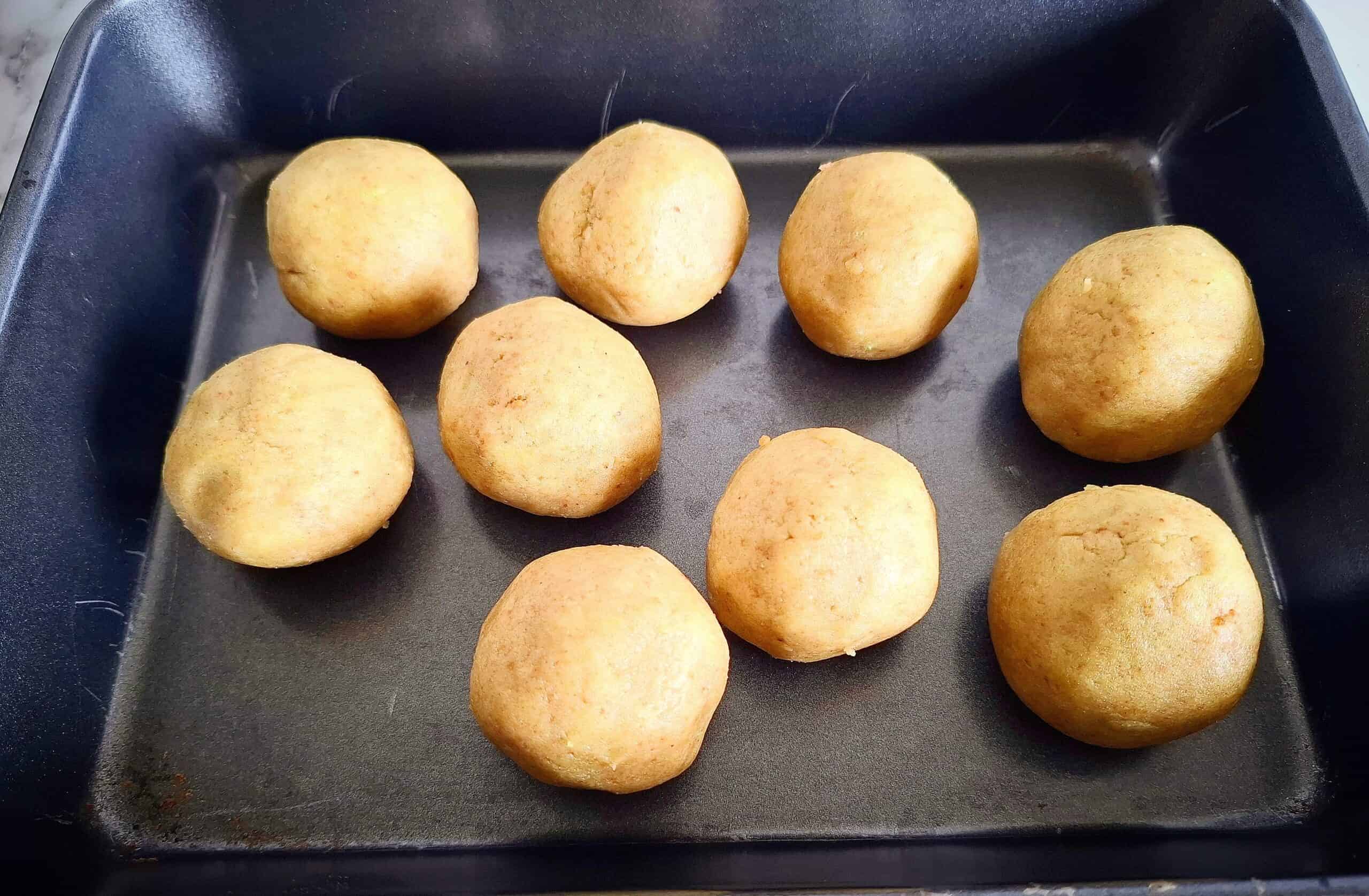 Nine un coated cake ball truffles in a black sheet pan.